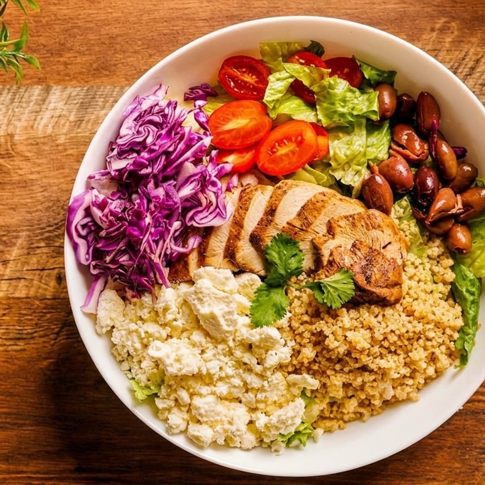 Overhead view of a colorful grilled chicken salad with quinoa, red cabbage, tomatoes, beans, lettuce, and cheese on a wooden table.