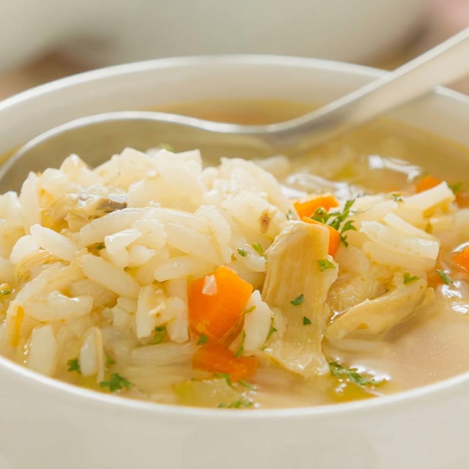 Bowl of chicken and rice soup with carrots, herbs, and a spoon resting across the rim.